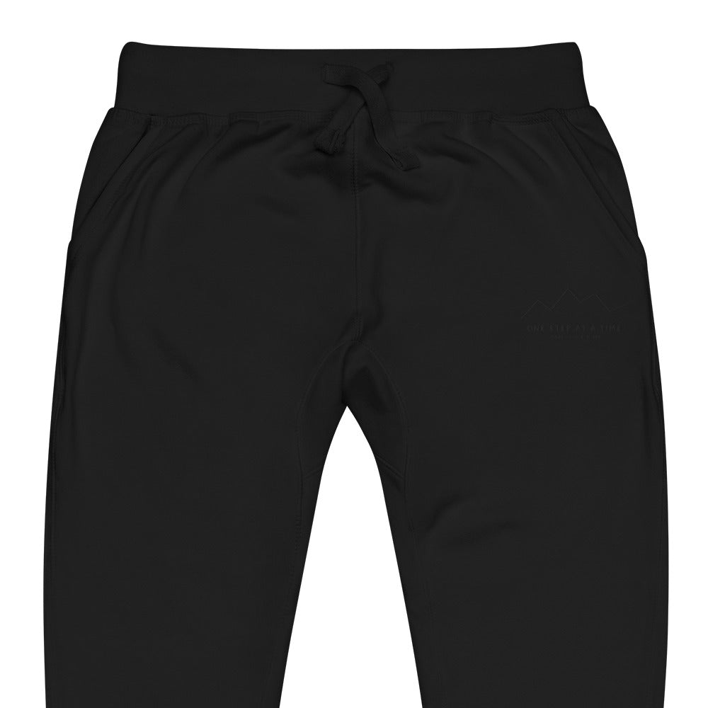 One Step at a Time Joggers in Black — close-up of the embroidered One Step at a Time logo at the left thigh