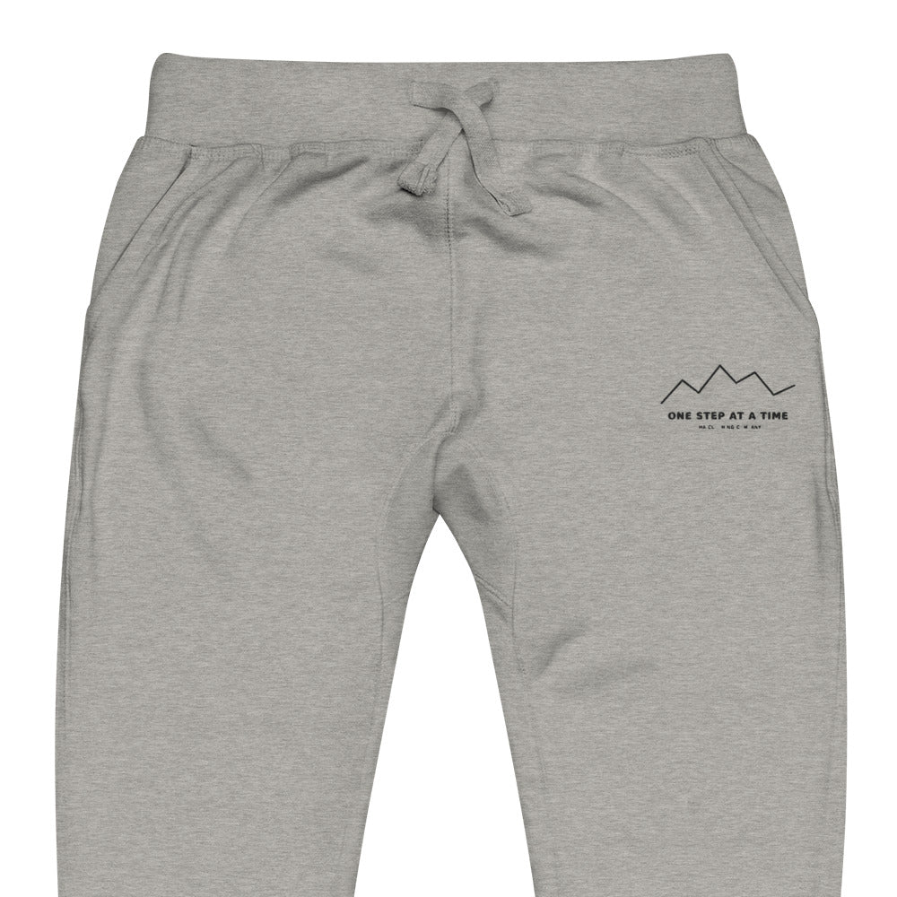 One Step at a Time Joggers in Carbon Grey — close-up of the embroidered One Step at a Time logo at the left thigh